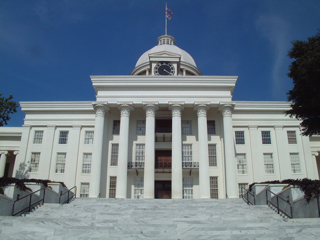 A wide shot of the white Alabama State Capitol building in Montgomery under a clear blue sky.